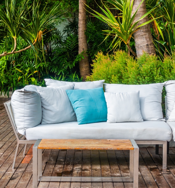 Terrasse en bois avec canapé d’extérieur, végétation dense et ambiance exotique, pour un aménagement paysager propice à la détente